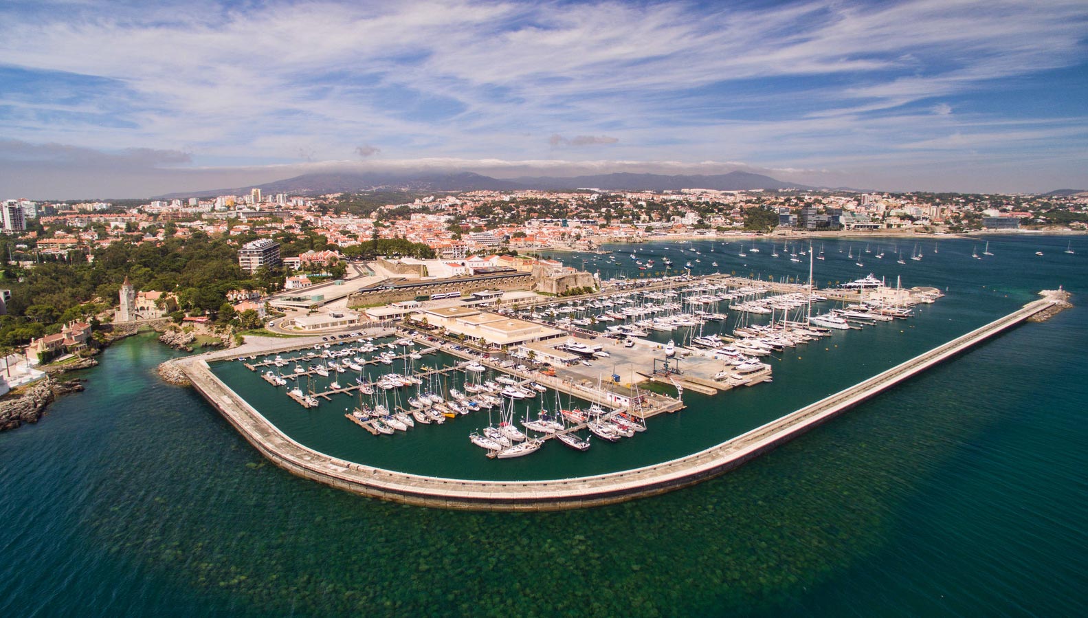 Panoramic view of Cascais marina at golden hour, with luxury yachts, waterfront restaurants, and historic architecture creating an elegant ambiance.